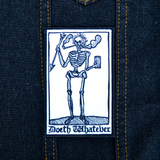 Rectangular black and white embroidered patch of a smoking skeleton in a medieval woodcut design style with the phrase doeth whatever spelled out in old English lettering. Shown on a denim jacket.