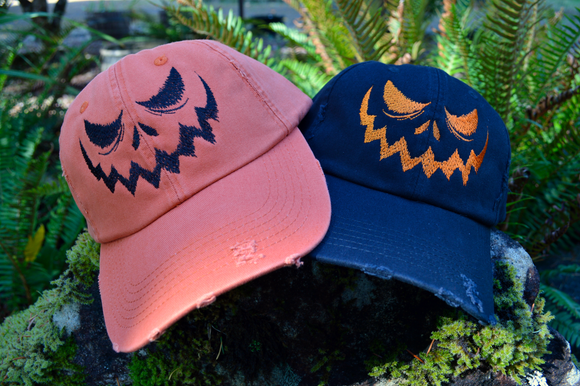Two hats, one orange and one black, with a jack o lantern face embroidered on the front.