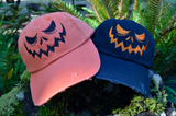 Two hats, one orange and one black, with a jack o lantern face embroidered on the front.