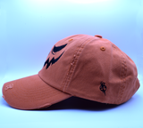 The side of an orange baseball style hat with a pumpkin jack o lantern face embroidered on the front in black thread.