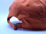 The back of an orange baseball style hat with an adjustable metal buckle.