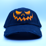 A black baseball style hat with a pumpkin jack o lantern face embroidered on the front in orange thread.