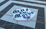 A white badge-shaped embroidered patch with silver border, purple flowers and the phrase, got the morbs, written in old english typesetting.