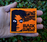 Rectangular orange and black embroidered patch for the classic horror movie black sunday. Shown in the palm of a hand for size reference.