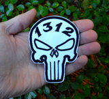 Black and white embroidered Punisher symbol patch with the number 1312, held in the palm of a hand.