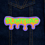 A purple, orange, and neon green embroidered patch shaped like dripping ooze with the word slimebag.