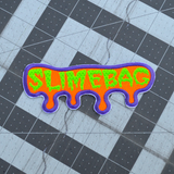 A purple, orange, and neon green embroidered patch shaped like dripping ooze with the word slimebag.