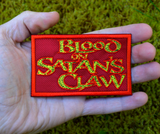 Rectangular red patch with textured yellow text 'Blood on Satan's Claw', inspired by the classic folk horror movie. Shown in the palm of a hand for size reference.