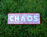 Rectangular embroidered patch with the word chaos cut out of random lines of red thread on white fabric.