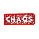 A rectangular red bordered embroidered patch on white fabric with the word chaos carved out of a web of random lines of red thread.