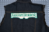 Rectangular embroidered patch resembling a wooden sign with the logo of the Arkham Horror board and card games. Shown on the back of a denim vest.