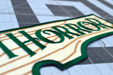 Close up detail of rectangular embroidered patch resembling a wooden sign with the logo of the Arkham Horror board and card games.