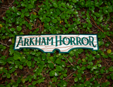 Rectangular embroidered patch resembling a wooden sign with the logo of the Arkham Horror board and card games.