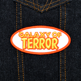 An oval-shaped white, orange, and yellow embroidered patch made from the title logo of the cult classic sci-fi horror movie Galaxy of Terror.