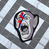 An embroidered patch of the Bat Boy from the classic Weekly World News tabloid with a David Bowie red and blue lightening bolt painted on his face.