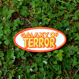 An oval-shaped white, orange, and yellow embroidered patch made from the title logo of the cult classic sci-fi horror movie Galaxy of Terror.