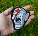 An embroidered patch of the Bat Boy from the classic Weekly World News tabloid with a David Bowie red and blue lightening bolt painted on his face. Shown in the palm of a hand for size reference.