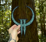 Embroidered patch made from the logo of the classic first person shooter video game Quake 2. Shown being held in a hand for size reference.