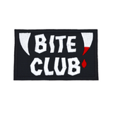 Rectangular black embroidered patch with the words bite club sewn in white thread with a pair of fangs on either side, one of which is dripping blood.