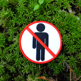 Circular white embroidered patch with red border and a red line crossing out a black silhouette of a person, resembling a public sign.