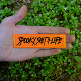 Rectangular orange embroidered patch with the text, spooky shit 4 life, stitched in black thread. Shown in the palm of a hand for size reference.