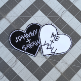 Two heart-shaped embroidered patches with personalized names for couples. One is white stitching on black fabric, one is black stitching on white fabric.