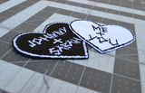 Close up detail of two heart-shaped embroidered patches with personalized names for couples. One is white stitching on black fabric, one is black stitching on white fabric.