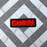 Black rectangular embroidered patch with the name Gamera in red thread, based on the classic Japanese Kaiju monster movie.