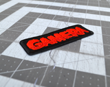 Close up detail of a black rectangular embroidered patch with the name Gamera in red thread, based on the classic Japanese Kaiju monster movie.