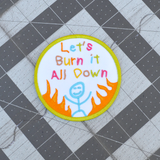 Circular patch with text 'Let's Burn it All Down' with a happy stick figure and flames on a white background and green border.