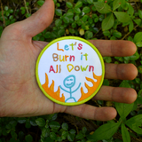 Circular patch with text 'Let's Burn it All Down' with a happy stick figure and flames on a white background and green border. Shown in the palm of a hand for size reference.