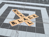 Close up detail of an embroidered patch that says black metal spelled out in Scrabble letters in the shape of an inverted cross.