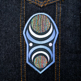 An oblong embroidered patch with abstract geometric arcs and circles in grey, black, and multi-color thread.