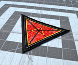 Close up detail of a triangular embroidered patch with a black border, textured red background and geometric designs in silver and gold metallic thread.