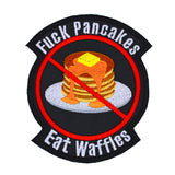 A round-shaped embroidered patch with a red circle and slash over a plate of pancakes surrounded by the words, fuck pancakes, eat waffles.