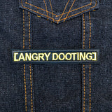 Rectangular black embroidered patch with yellow lettering that says angry dooting, resembling a movie subtitle.
