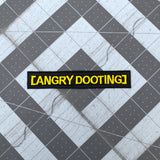 Rectangular black embroidered patch with yellow lettering that says angry dooting, resembling a movie subtitle.