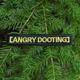 Rectangular black embroidered patch with yellow lettering that says angry dooting, resembling a movie subtitle.