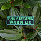 A rectangular embroidered patch on black fabric and a green border, with the words 'the future was a lie' in green block letters.