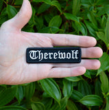 Black rectangular embroidered patch with the word 'therewolf' stitched with white thread in Old English lettering. Shown in the palm of a hand for size reference.