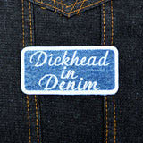 A rectangular embroidered patch on denim fabric with a white border and white lettering that reads, 'Dickhead in denim'.