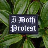A rectangular black embroidered patch with white Gothic lettering that reads 'I Doth Protest'.