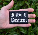 A rectangular black embroidered patch with white Gothic lettering that reads 'I Doth Protest'. Shown in the palm of a hand for size reference.