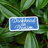 A rectangular embroidered patch on denim fabric with a white border and white lettering that reads, 'Dickhead in denim'.
