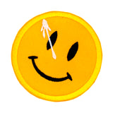 A circular yellow embroidered patch of a smiley face with a white splatter across its right eye.