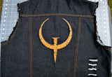 A large rust colored embroidered patch of the logo for the Quake 1 video game on the back of a denim vest.