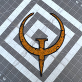 A large rust colored embroidered patch of the logo for the Quake 1 video game.