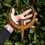 A large rust colored embroidered patch of the logo for the Quake 1 video game, held by a hand for size reference.