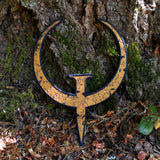 A large rust colored embroidered patch of the logo for the Quake 1 video game leaning against the trunk of a tree.