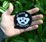 A black embroidered patch in the shape of a chat bubble with an evil-looking version of the reddit logo and the words, 'No Mods, No Masters'. Shown in the palm of a hand for size reference.